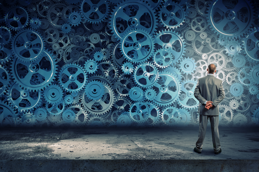 Back view of businessman looking at mechanism of cogwheels Back view of businessman looking at mechanism of cogwheels